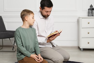 Photo of Muslim man and his son with Quran praying on mat at home