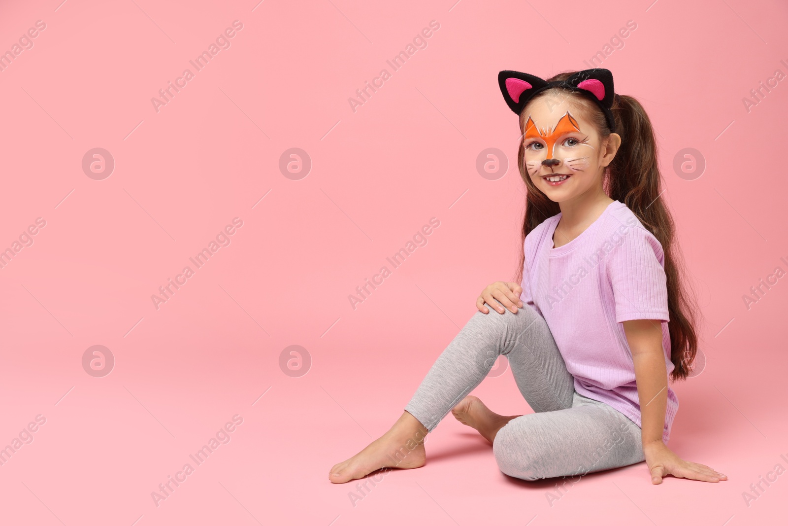 Photo of Cute girl with painted face and ears as cat on pink background, space for text