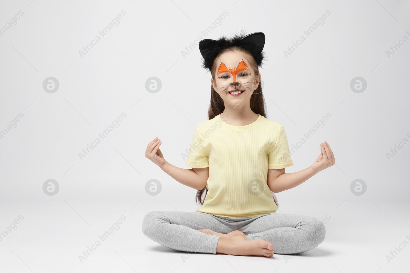 Photo of Cute girl with painted face and ears as cat on grey background, space for text