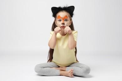 Photo of Cute girl with painted face and ears as cat on grey background