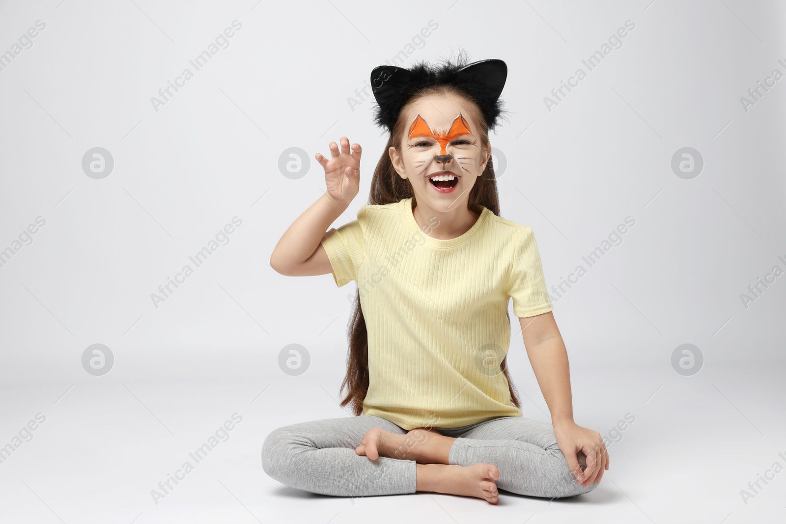 Photo of Cute girl with painted face and ears as cat on grey background