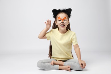 Photo of Cute girl with painted face and ears as cat on grey background