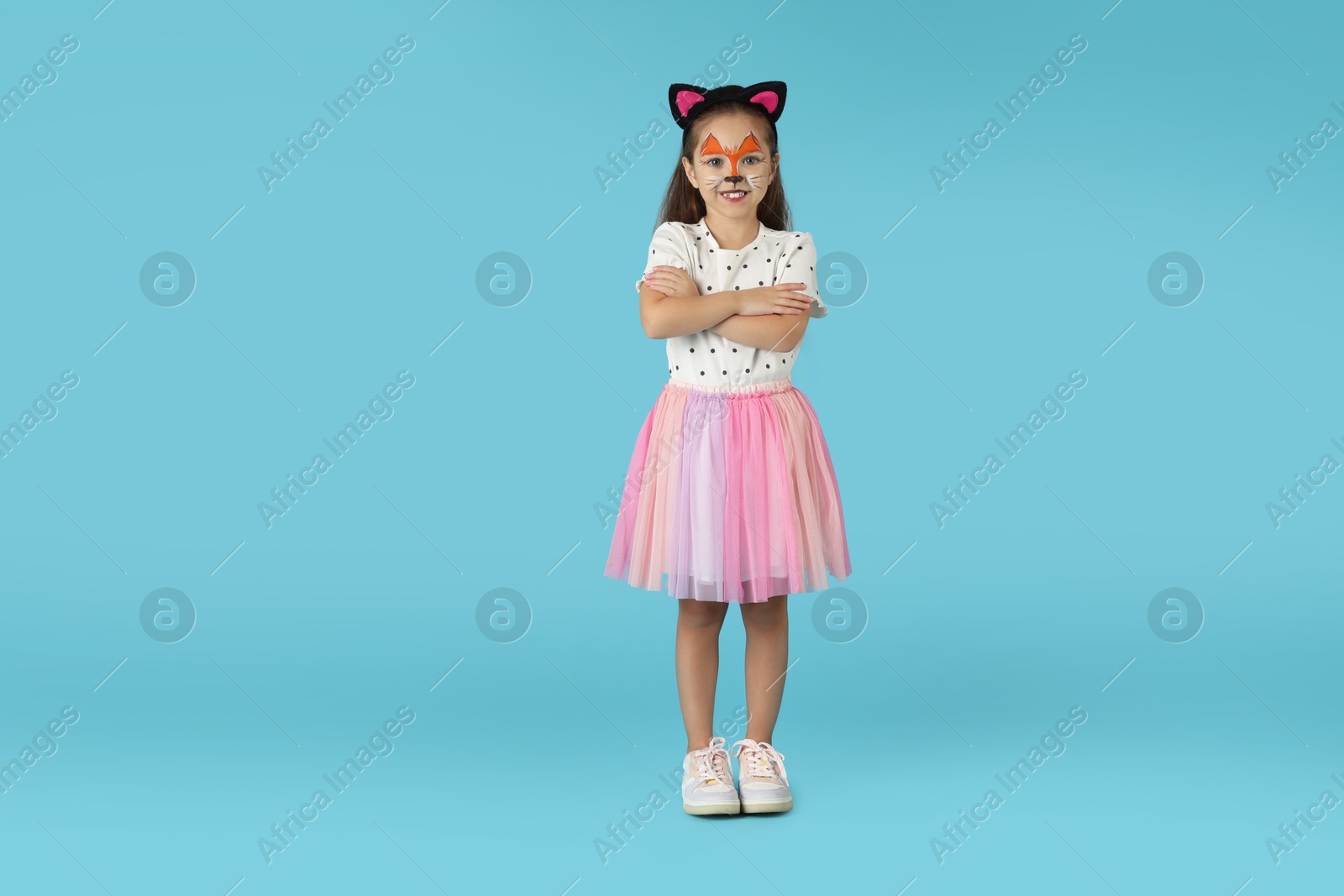 Photo of Cute girl with painted face and ears as cat on light blue background