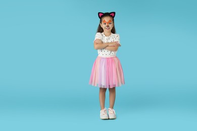 Photo of Cute girl with painted face and ears as cat on light blue background