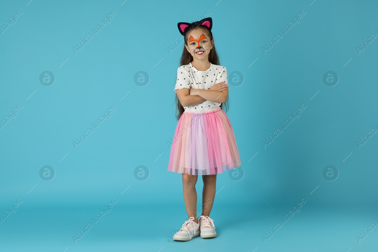 Photo of Cute girl with painted face and ears as cat on light blue background