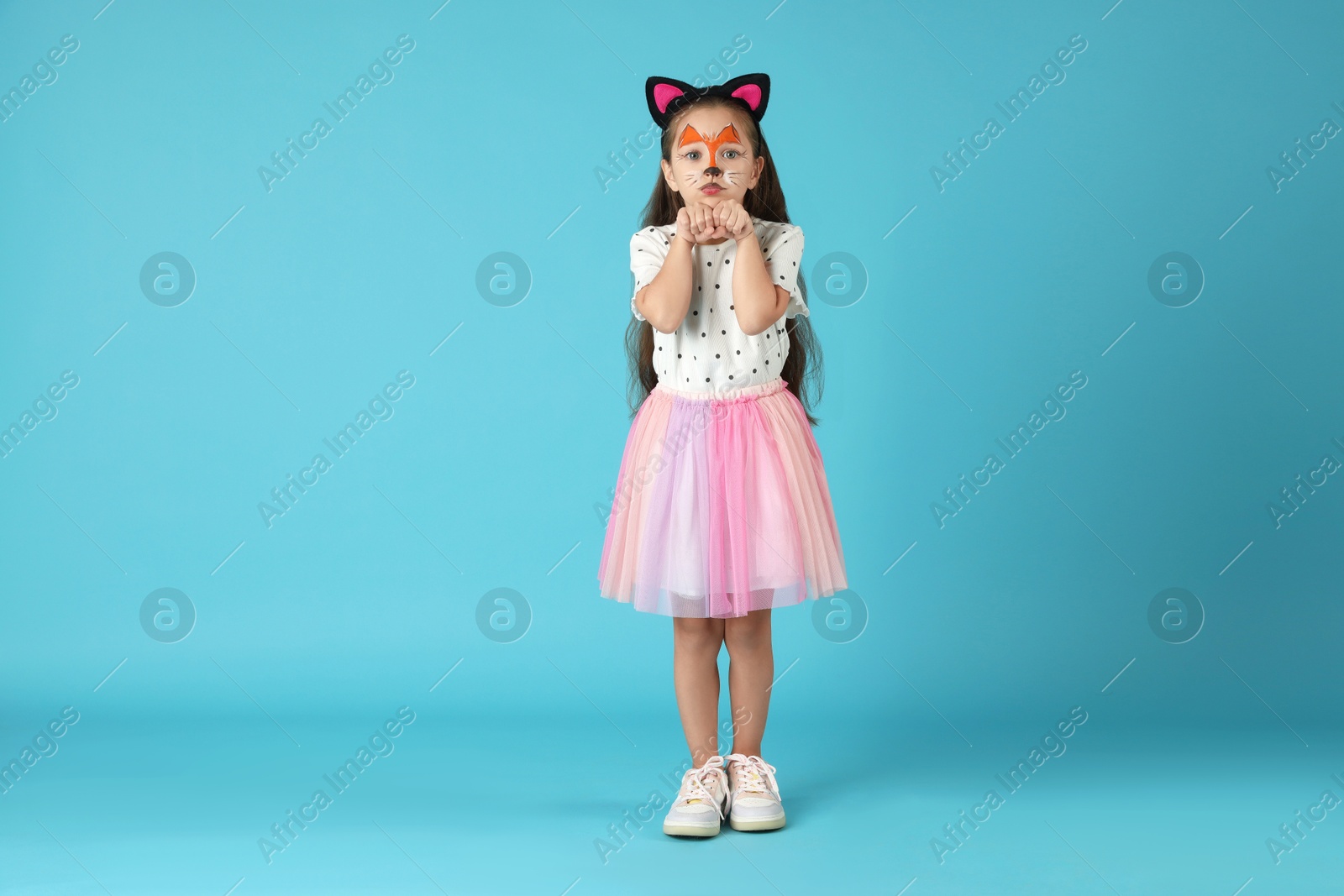 Photo of Cute girl with painted face and ears as cat on light blue background