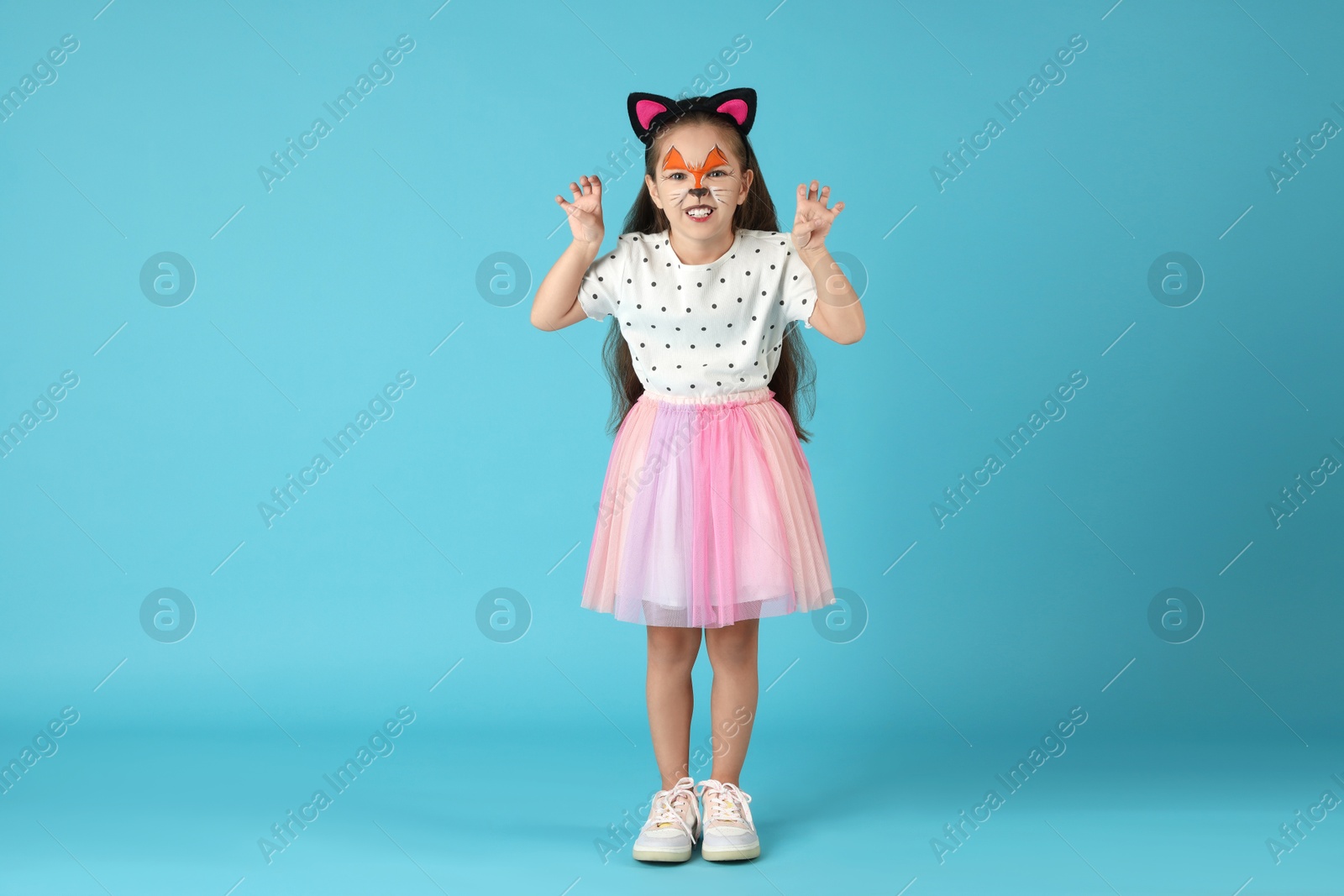 Photo of Cute girl with painted face and ears as cat on light blue background