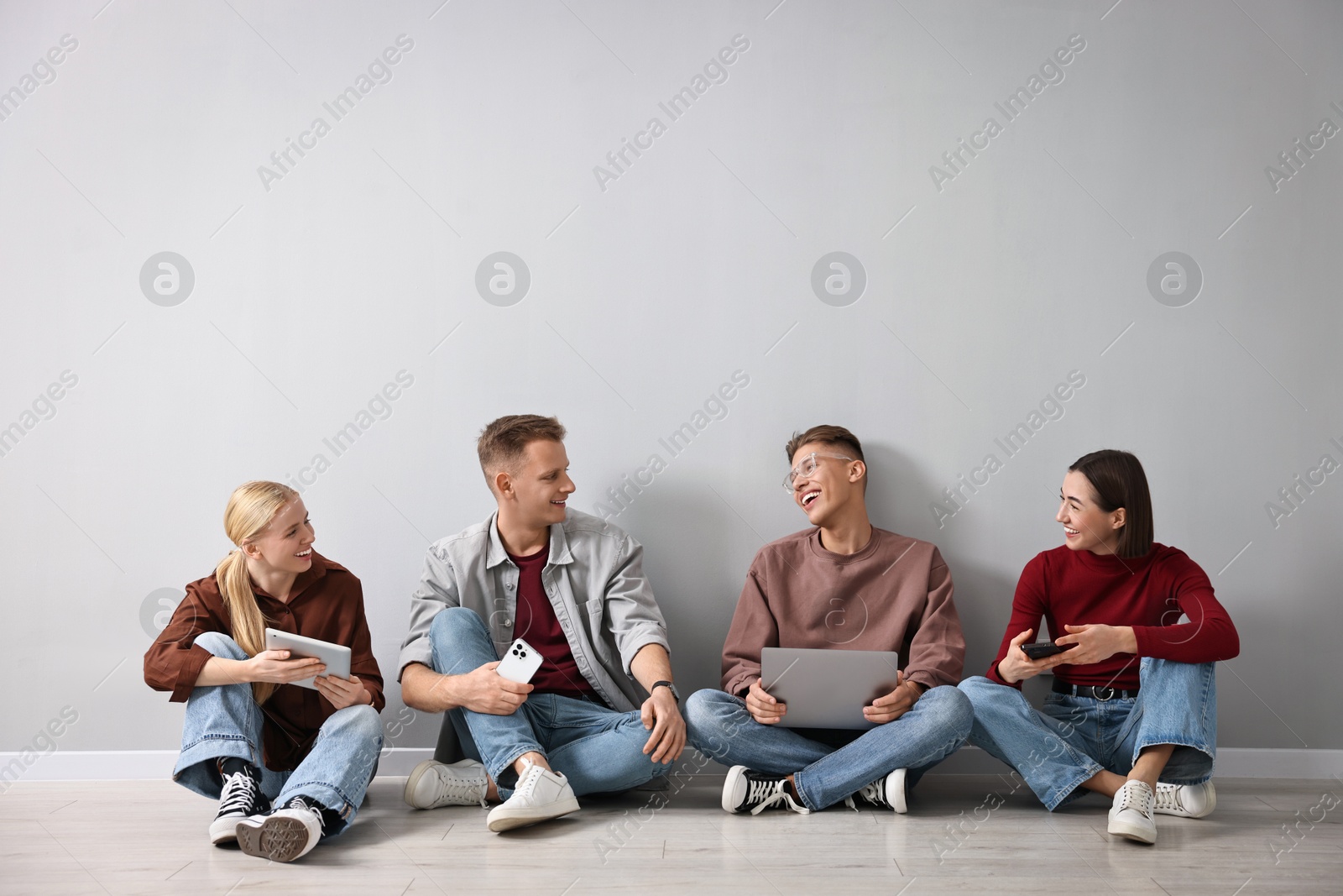 Photo of Group of people using different gadgets near light grey wall indoors. Modern technology