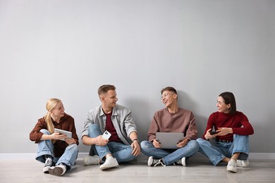 Photo of Group of people using different gadgets near light grey wall indoors. Modern technology