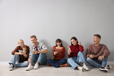 Photo of Group of people using different gadgets near light grey wall indoors. Modern technology