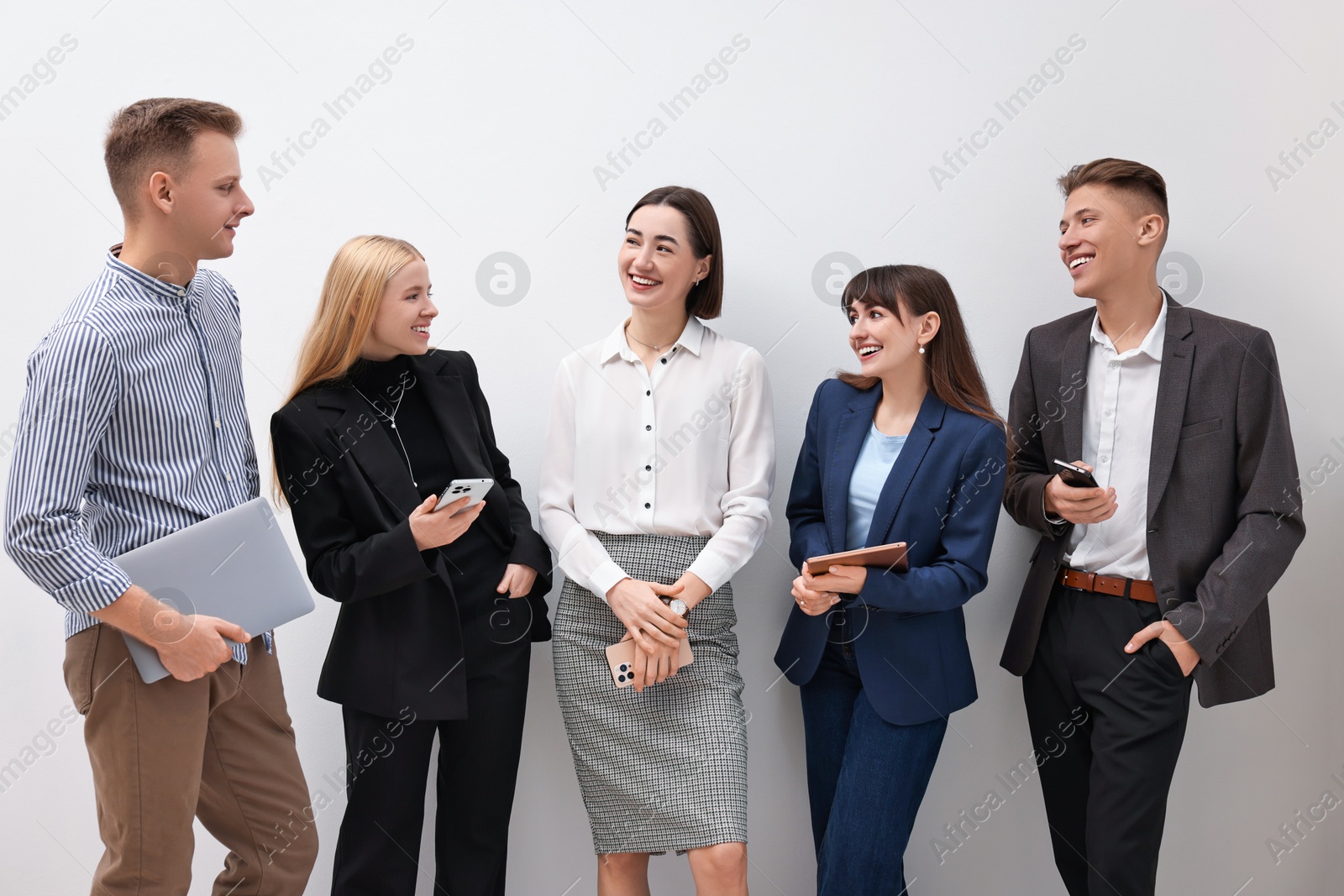 Photo of Group of people using different gadgets near white wall indoors. Modern technology