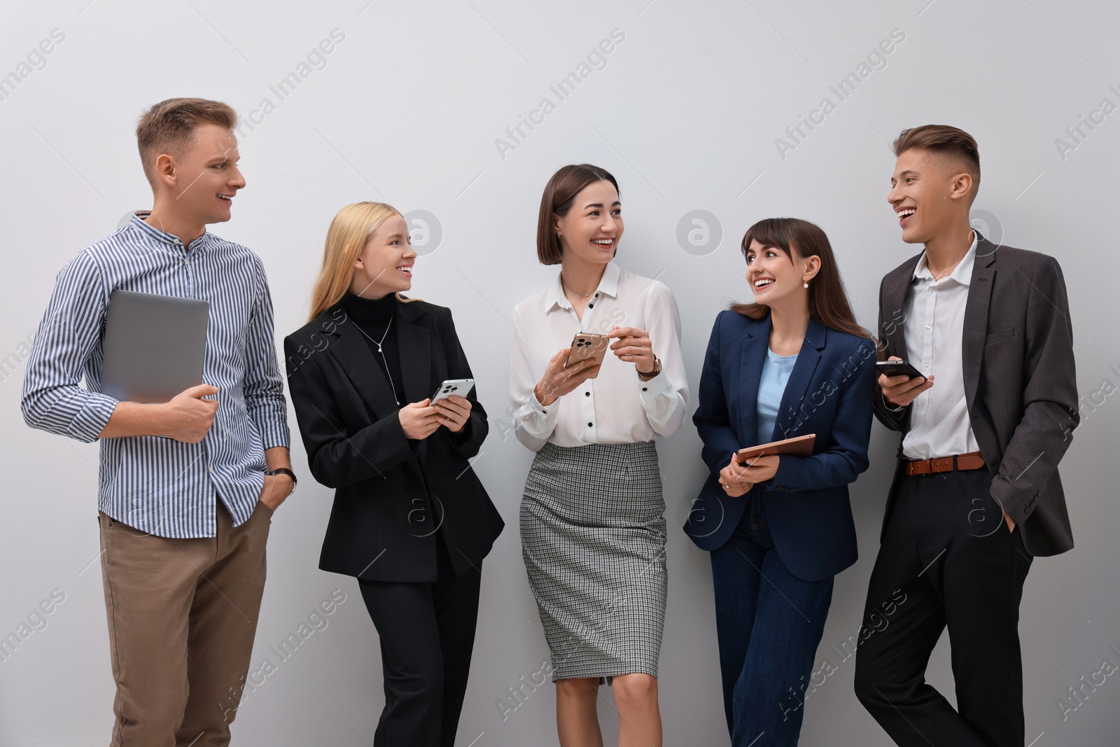 Photo of Group of people using different gadgets near white wall indoors. Modern technology