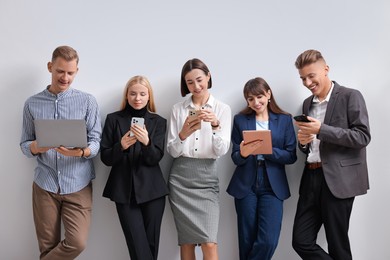 Photo of Group of people using different gadgets near white wall indoors. Modern technology