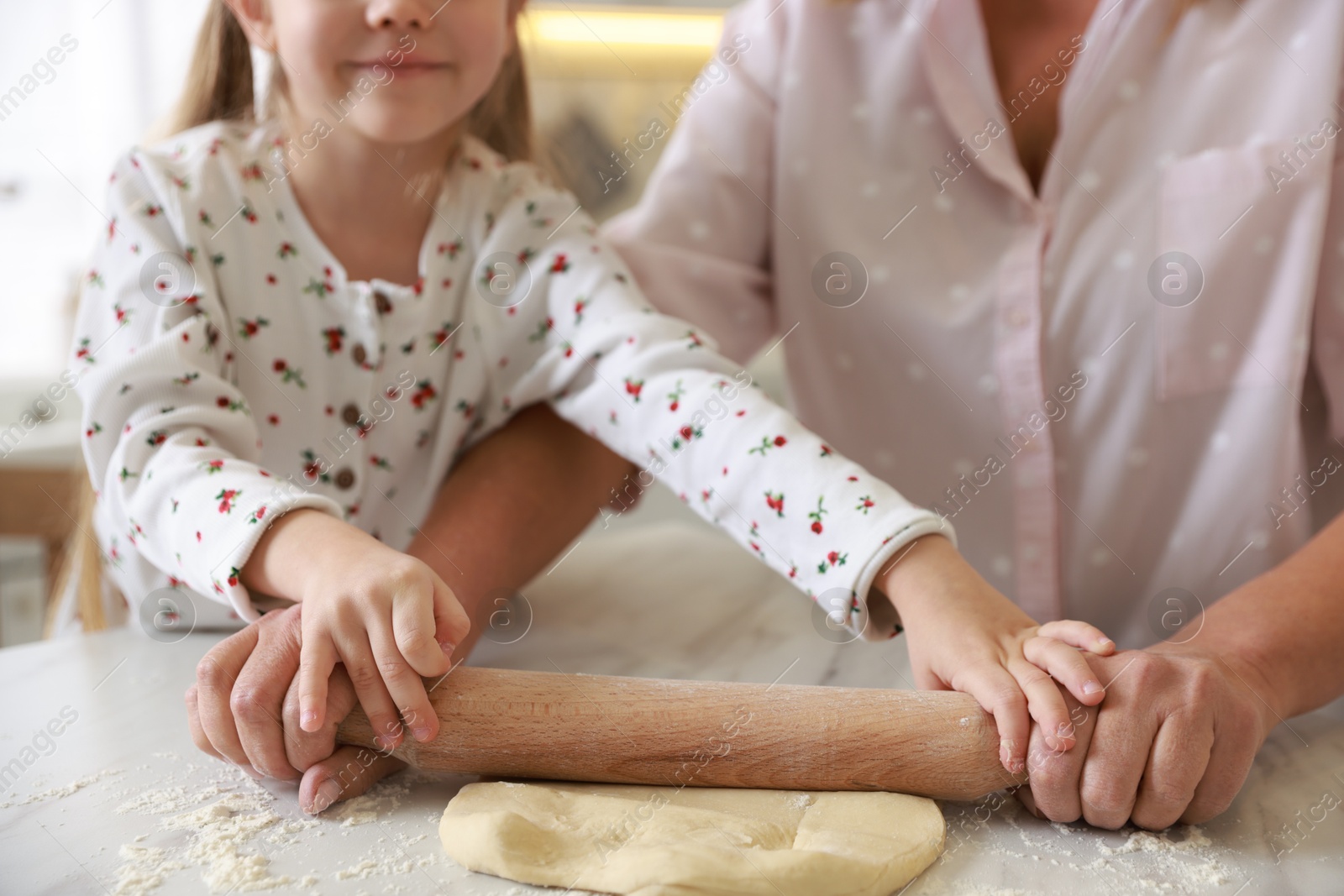 Photo of Grandmother and her granddaughter shaping dough with rolling pin at white marble table in kitchen, closeup