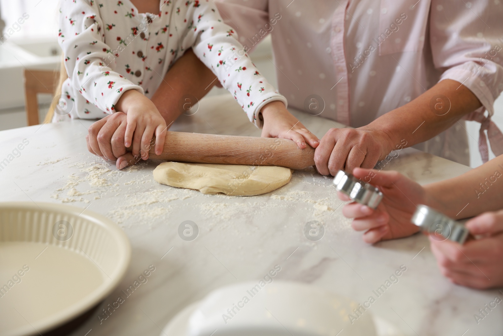 Photo of Grandmother and her grandchildren shaping dough with rolling pin at white marble table in kitchen, closeup