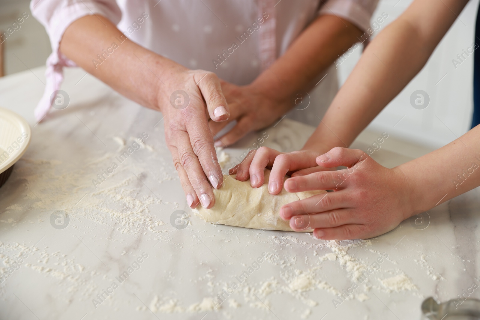 Photo of Grandmother and her grandson kneading dough at white marble table in kitchen, closeup