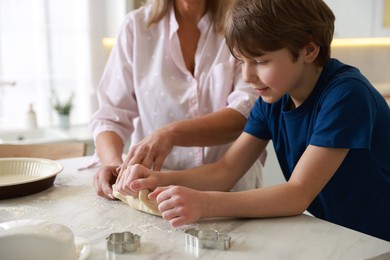 Photo of Grandmother and her grandson kneading dough at white marble table in kitchen