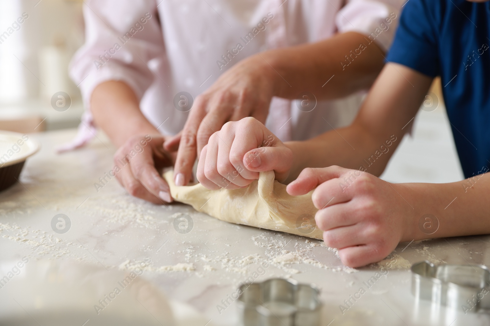 Photo of Grandmother and her grandson kneading dough at white marble table in kitchen, closeup