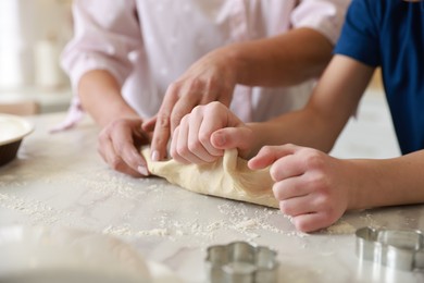 Photo of Grandmother and her grandson kneading dough at white marble table in kitchen, closeup