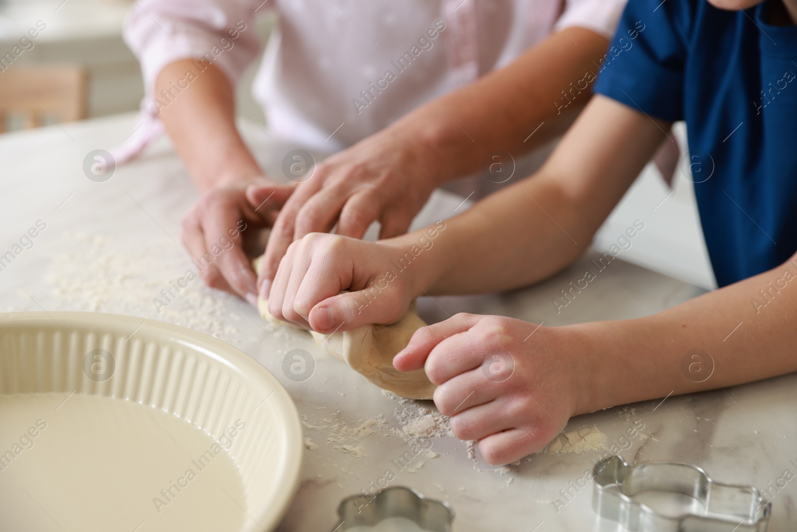 Photo of Grandmother and her grandson kneading dough at white marble table in kitchen