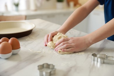 Photo of Boy kneading dough at white marble table in kitchen, closeup