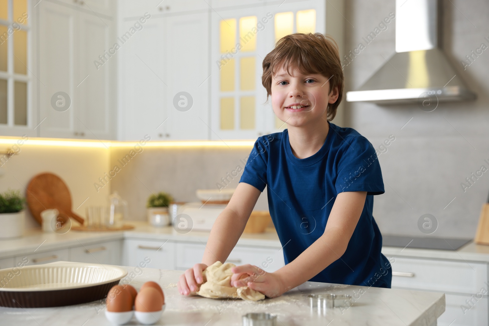 Photo of Cute boy kneading dough at white marble table in kitchen, space for text