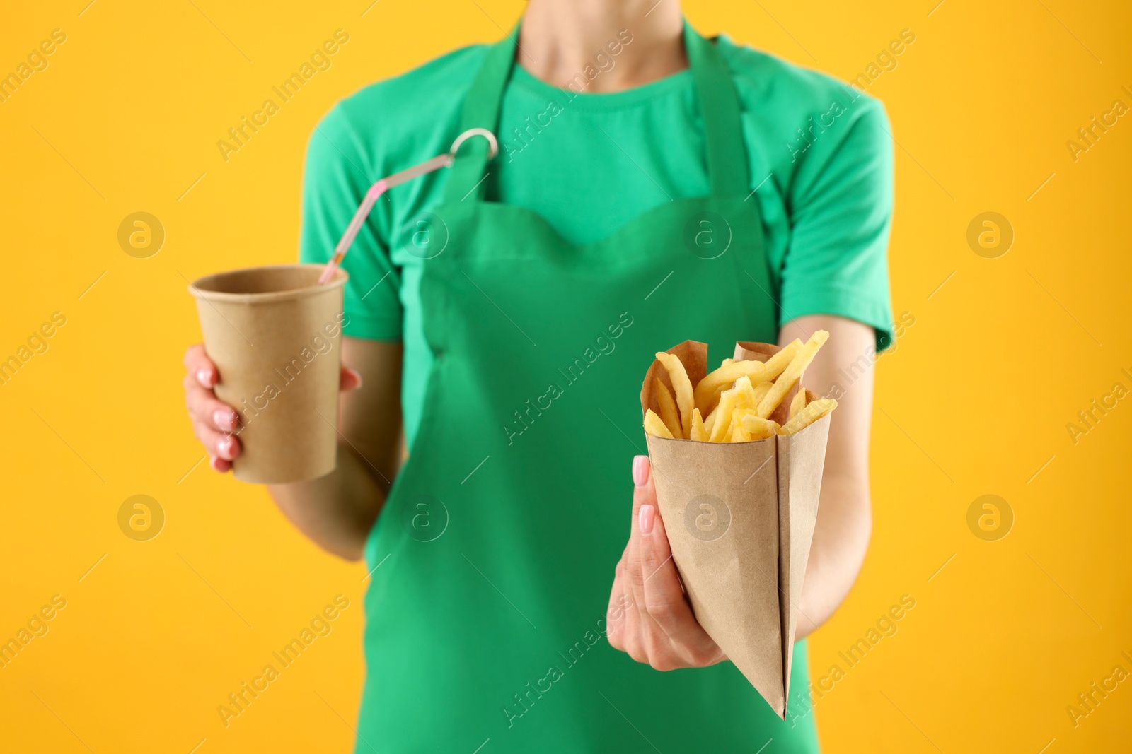 Photo of Fast-food worker with fries and paper cup on orange background, closeup