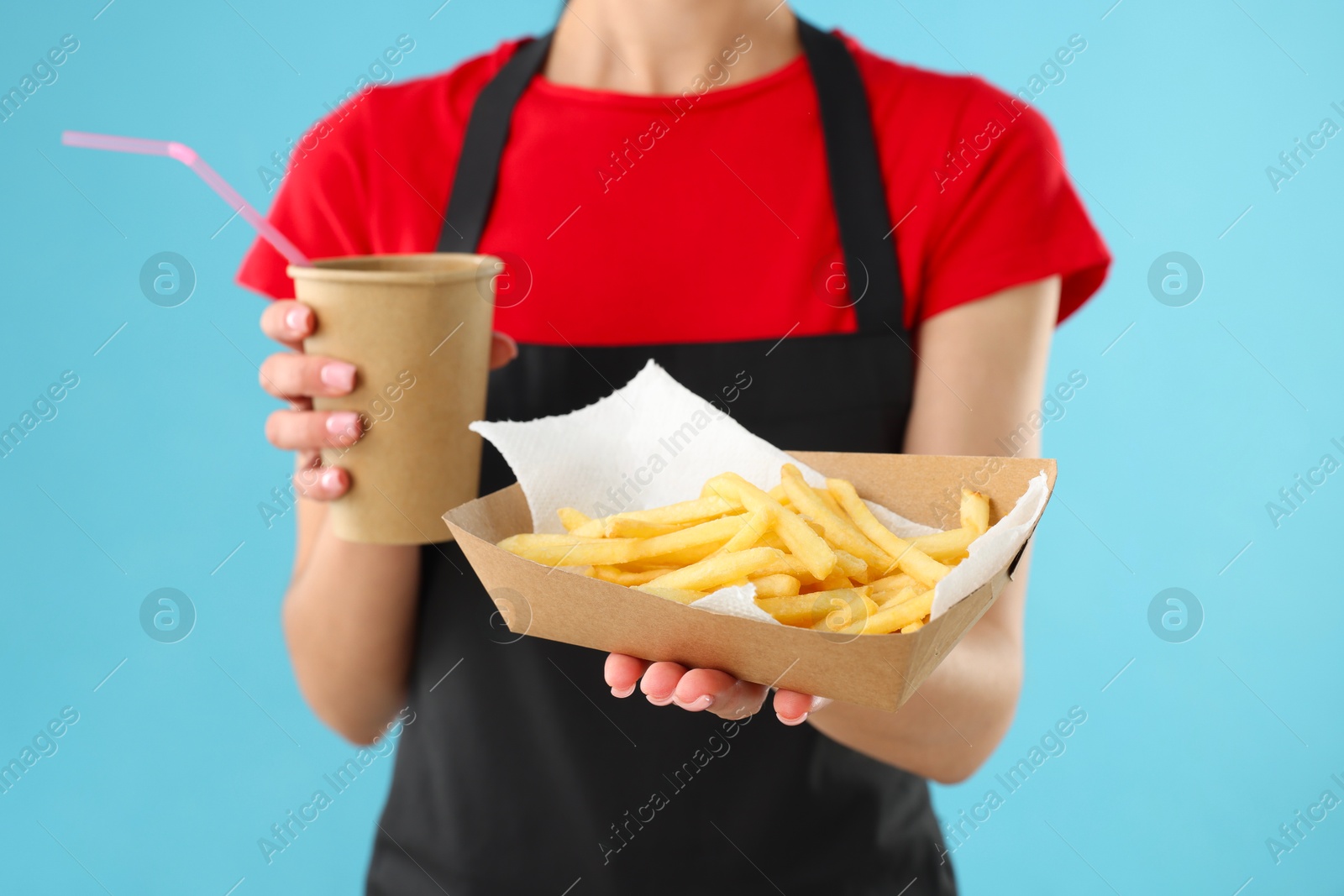 Photo of Fast-food worker with paper cup and fries on light blue background, closeup