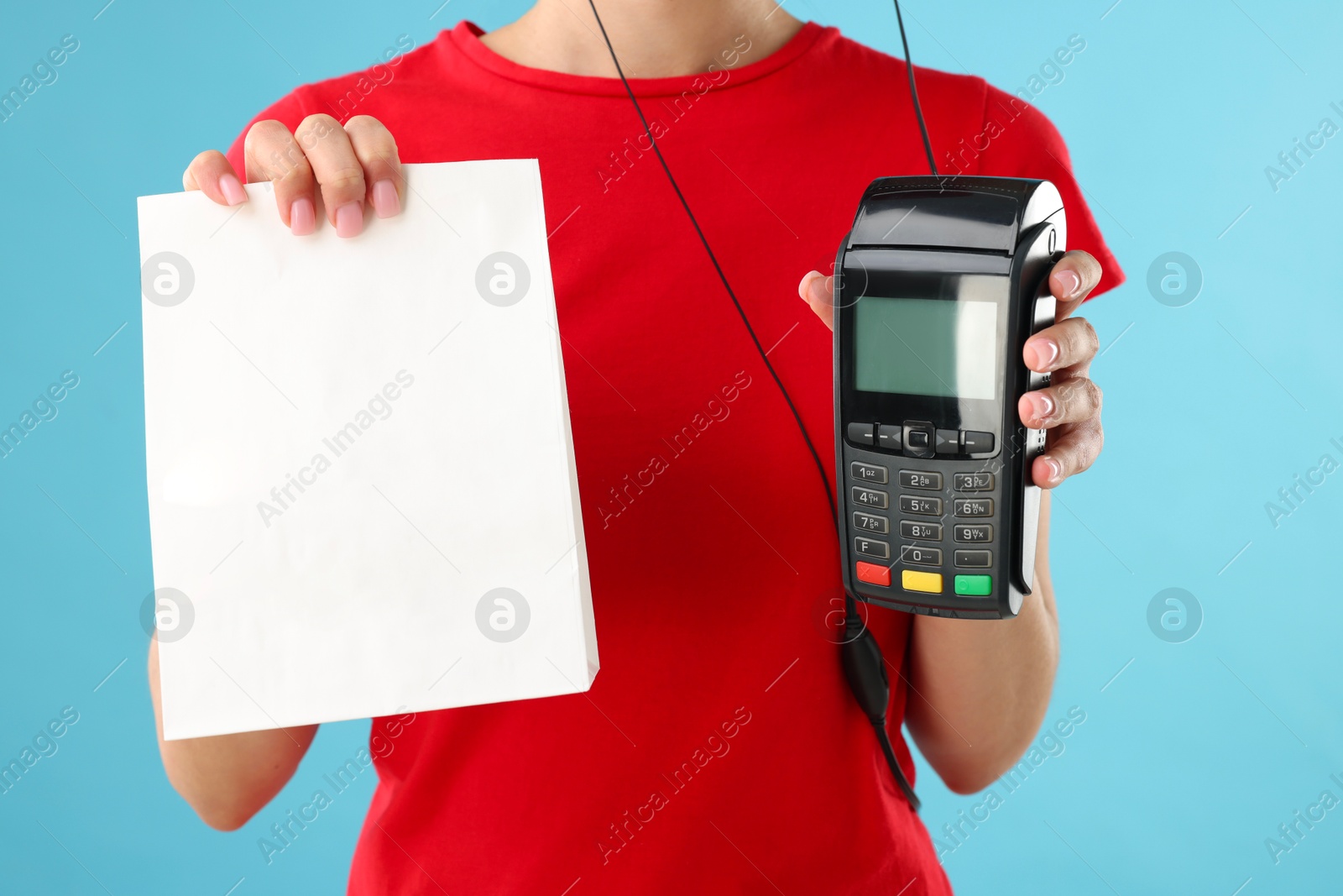 Photo of Fast-food worker with paper bag and payment terminal on light blue background, closeup