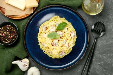 Photo of Plate with delicious pasta Carbonara, products and cutlery on grey textured table, flat lay