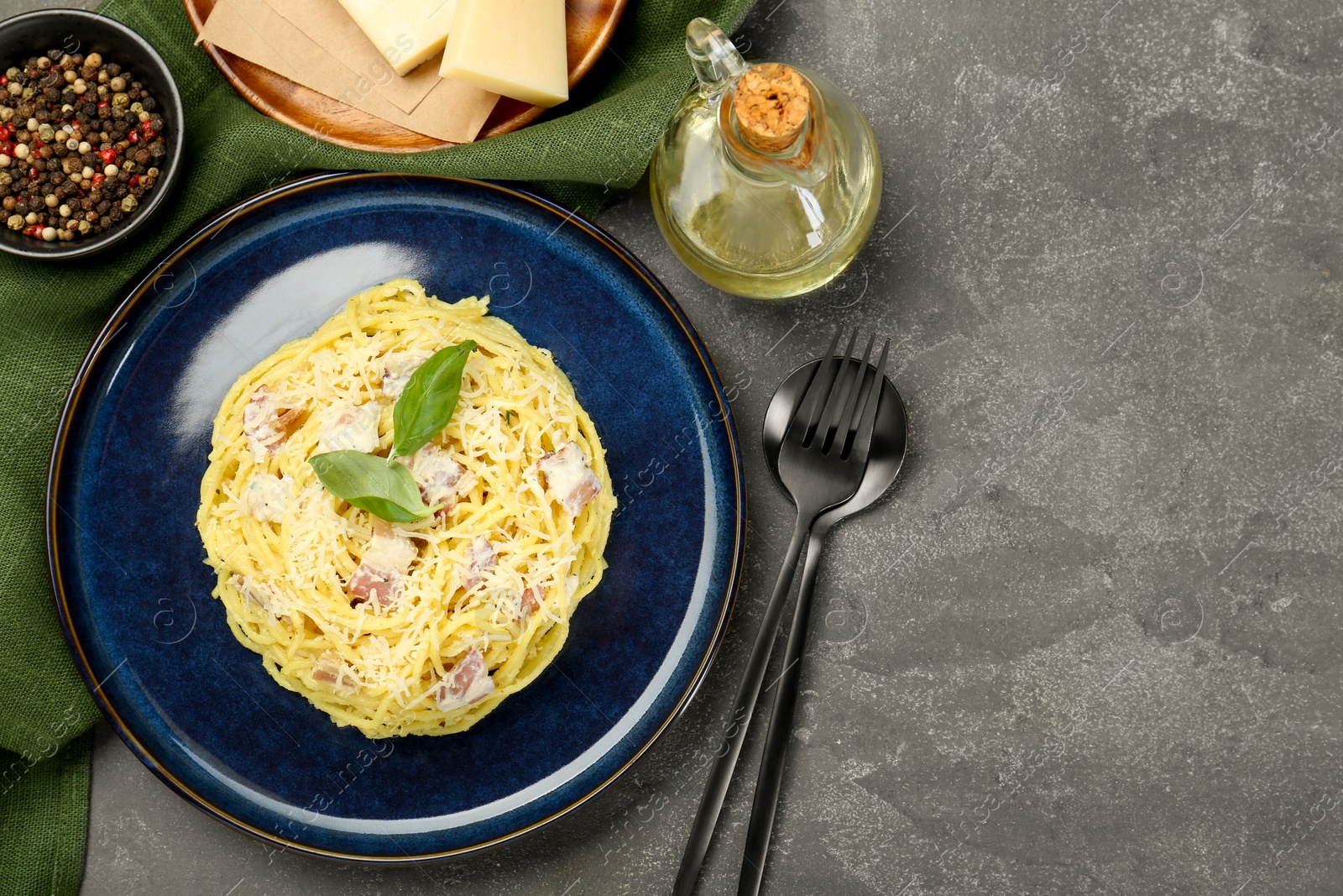 Photo of Plate with delicious pasta Carbonara, products and cutlery on grey textured table, flat lay. Space for text