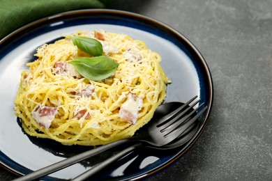 Photo of Plate with delicious pasta Carbonara and cutlery on grey textured table, closeup