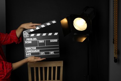 Photo of Woman with clapperboard near spotlight on black background, closeup