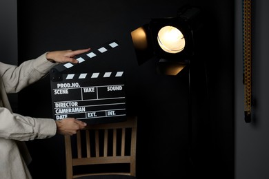 Photo of Woman with clapperboard near spotlight on black background, closeup