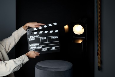 Photo of Woman with clapperboard near spotlight on black background, closeup