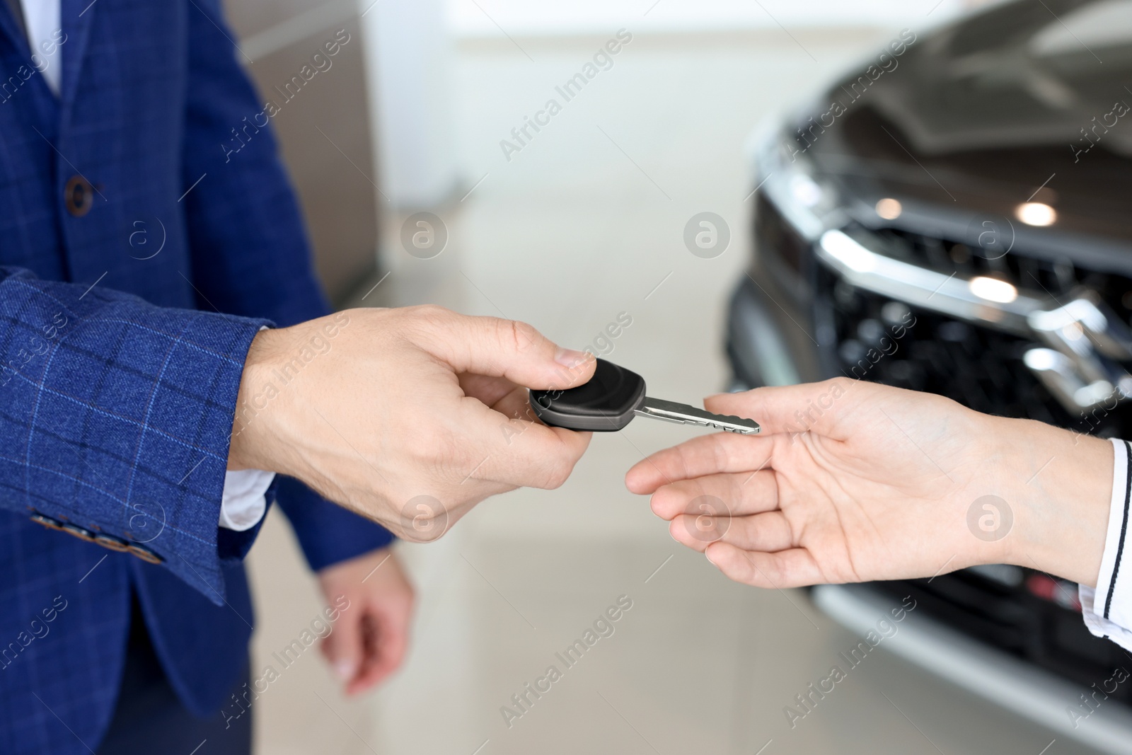 Photo of Salesman giving key to client near new car in salon, closeup