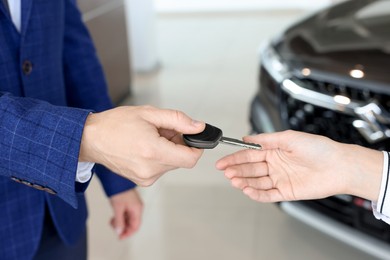 Photo of Salesman giving key to client near new car in salon, closeup