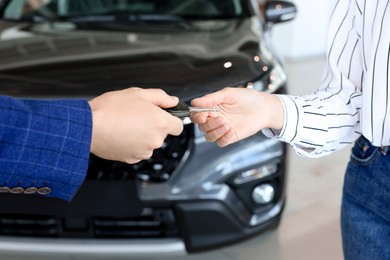 Photo of Salesman giving key to client near new car in salon, closeup