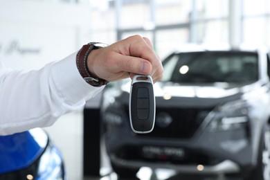 Photo of Salesman holding key near new car in salon, closeup