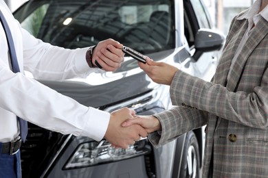 Photo of Salesman giving key to client near new car in salon, closeup