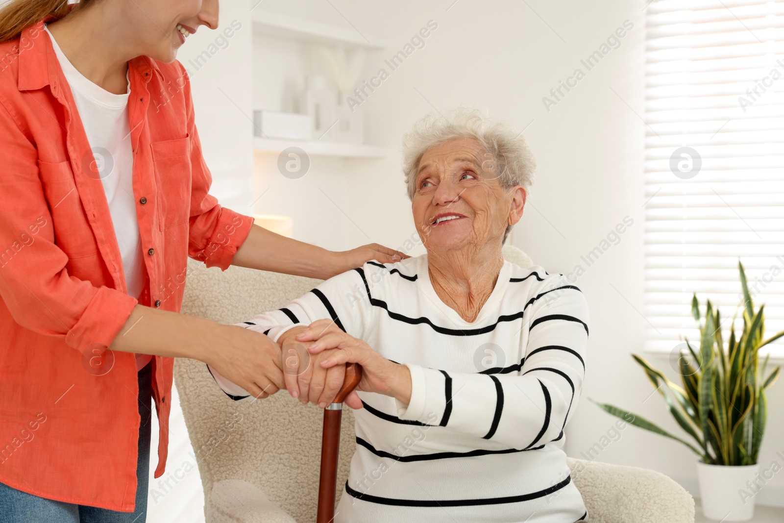 Photo of Caregiver supporting senior woman in living room at home