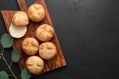 Photo of Homemade tasty buns and eucalyptus branch on black textured table, flat lay. Space for text