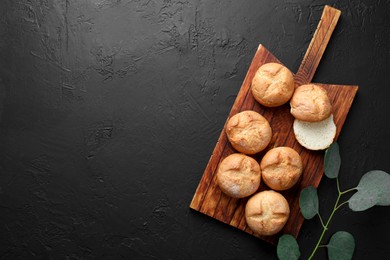 Photo of Homemade tasty buns and eucalyptus branch on black textured table, flat lay. Space for text