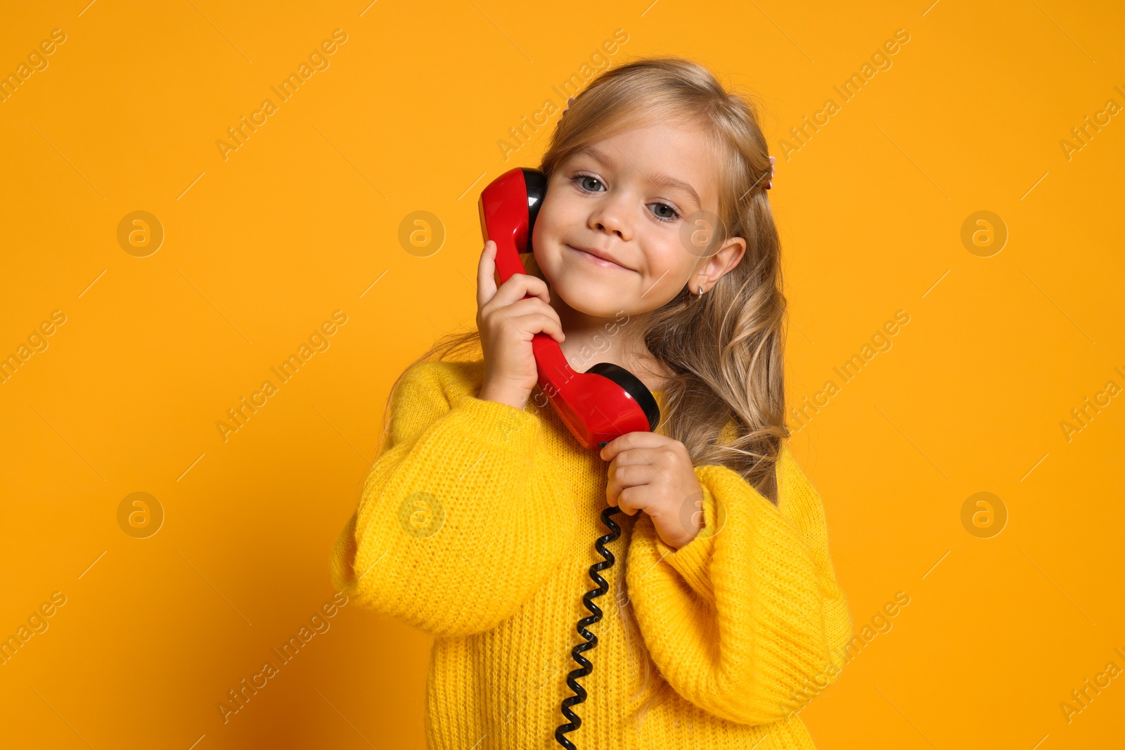 Photo of Cute little girl with handset of telephone on orange background