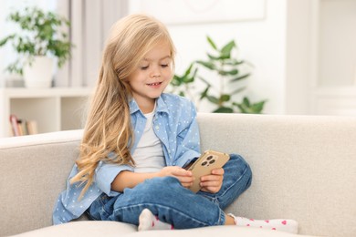 Photo of Cute little girl using smartphone on sofa at home