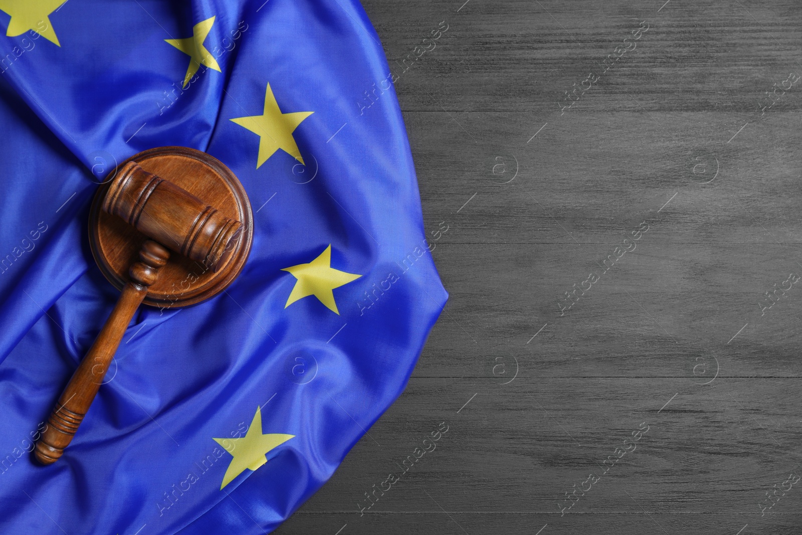 Photo of Judge's gavel and flag of European Union on grey wooden table, top view. Space for text