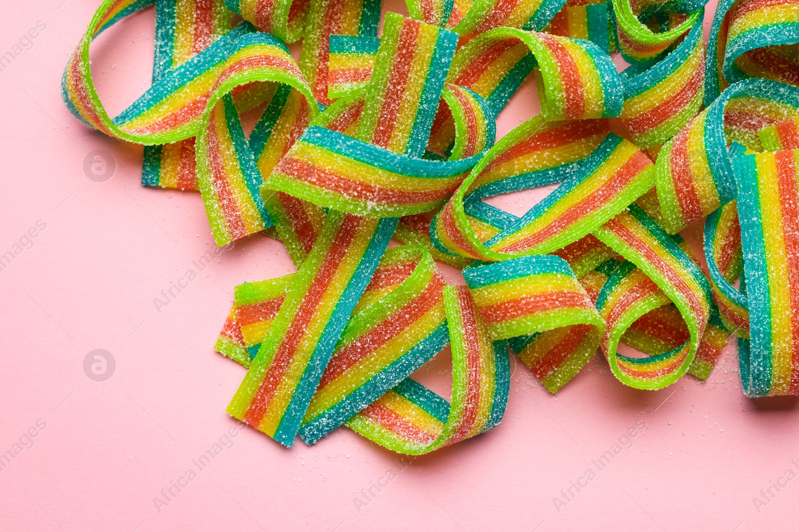 Photo of Tasty rainbow sour belts on pink background, top view