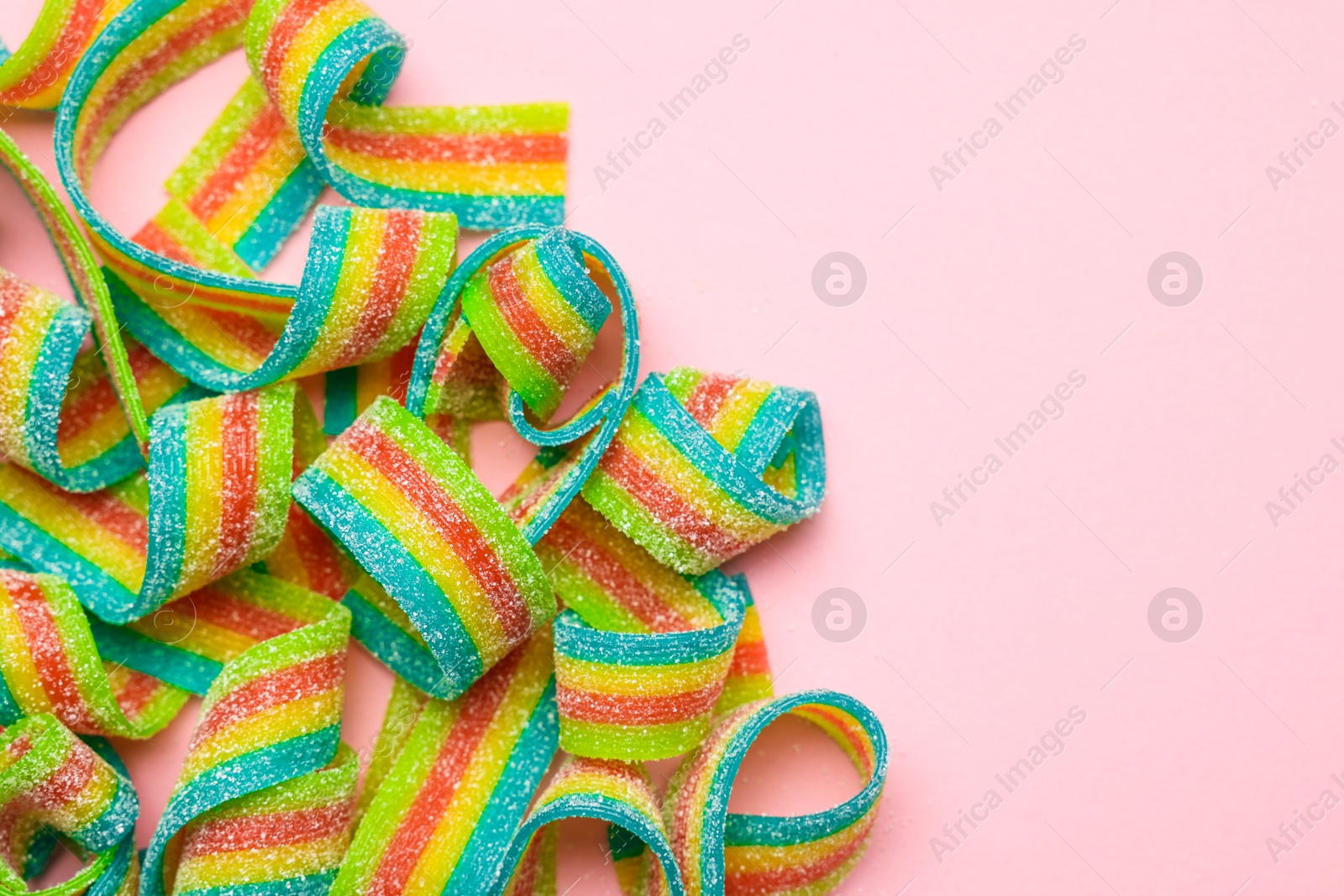 Photo of Tasty rainbow sour belts on pink background, top view. Space for text