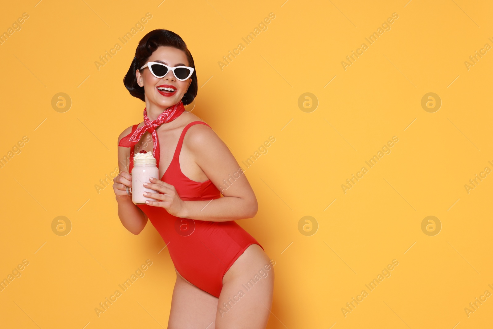 Photo of Pin-up woman in swimsuit with milk shake on orange background, space for text