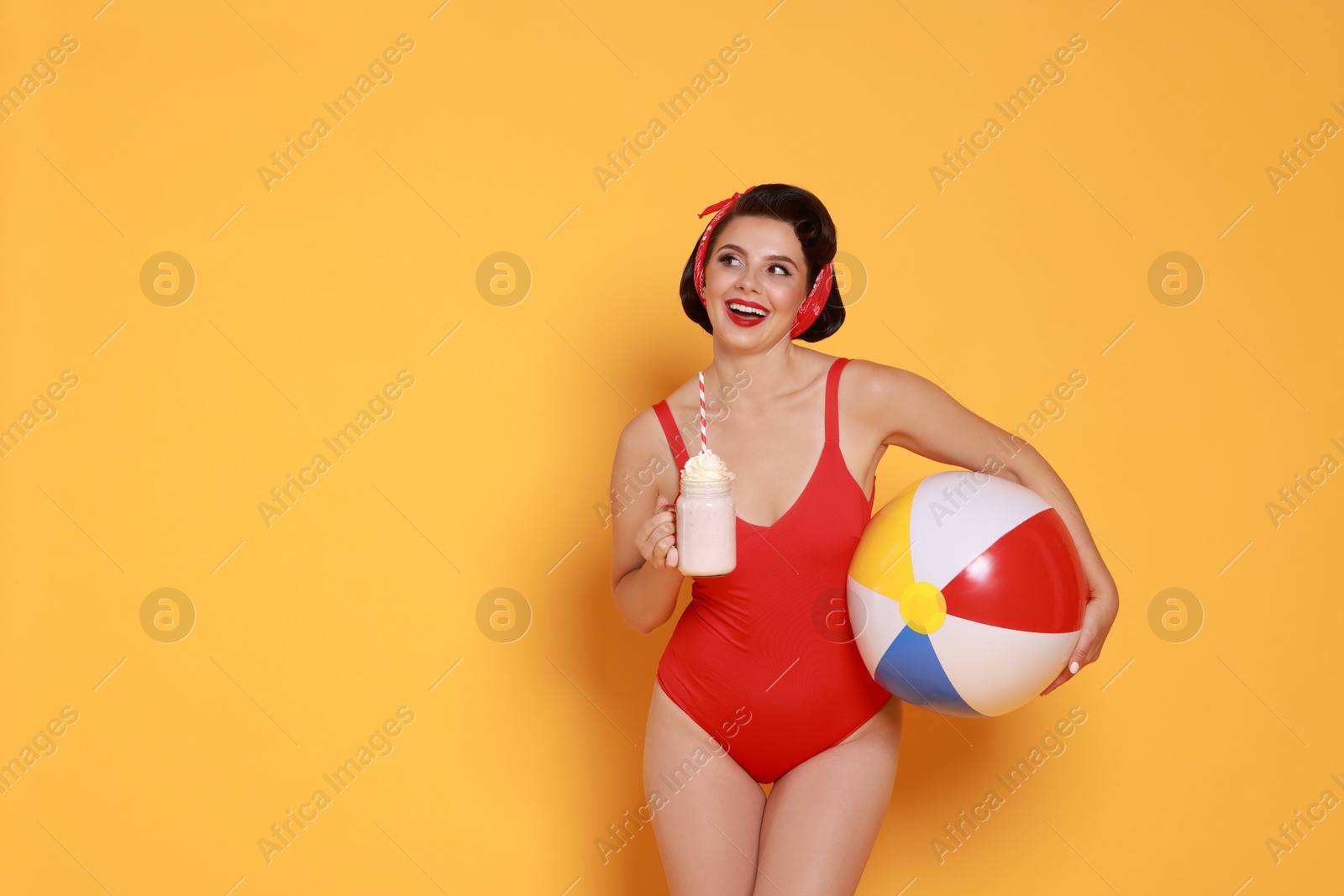 Photo of Pin-up woman in swimsuit with milk shake and inflatable ball on orange background, space for text